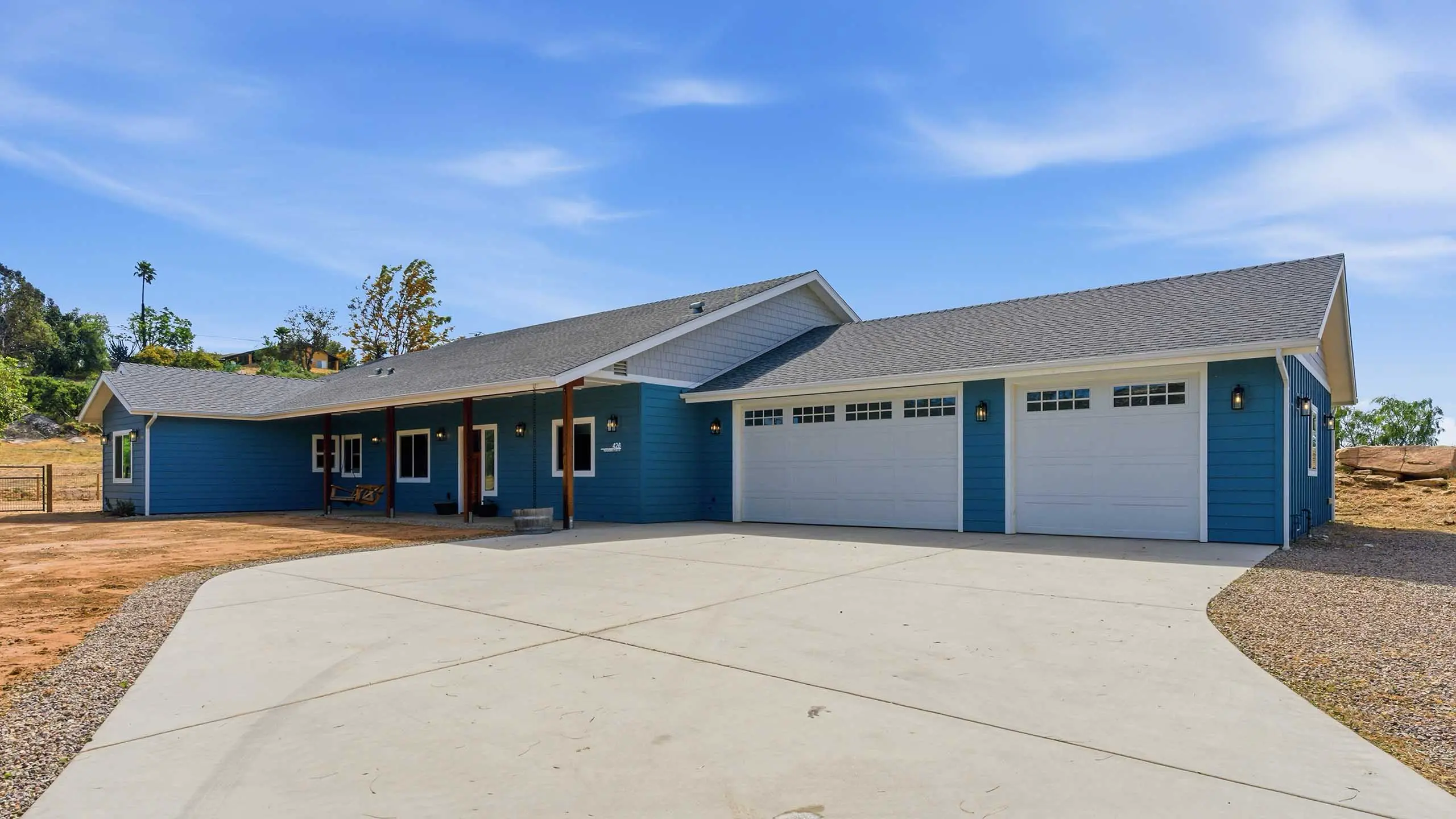 Blue single-story house with white garage doors and a wide concrete driveway beneath a clear blue sky.