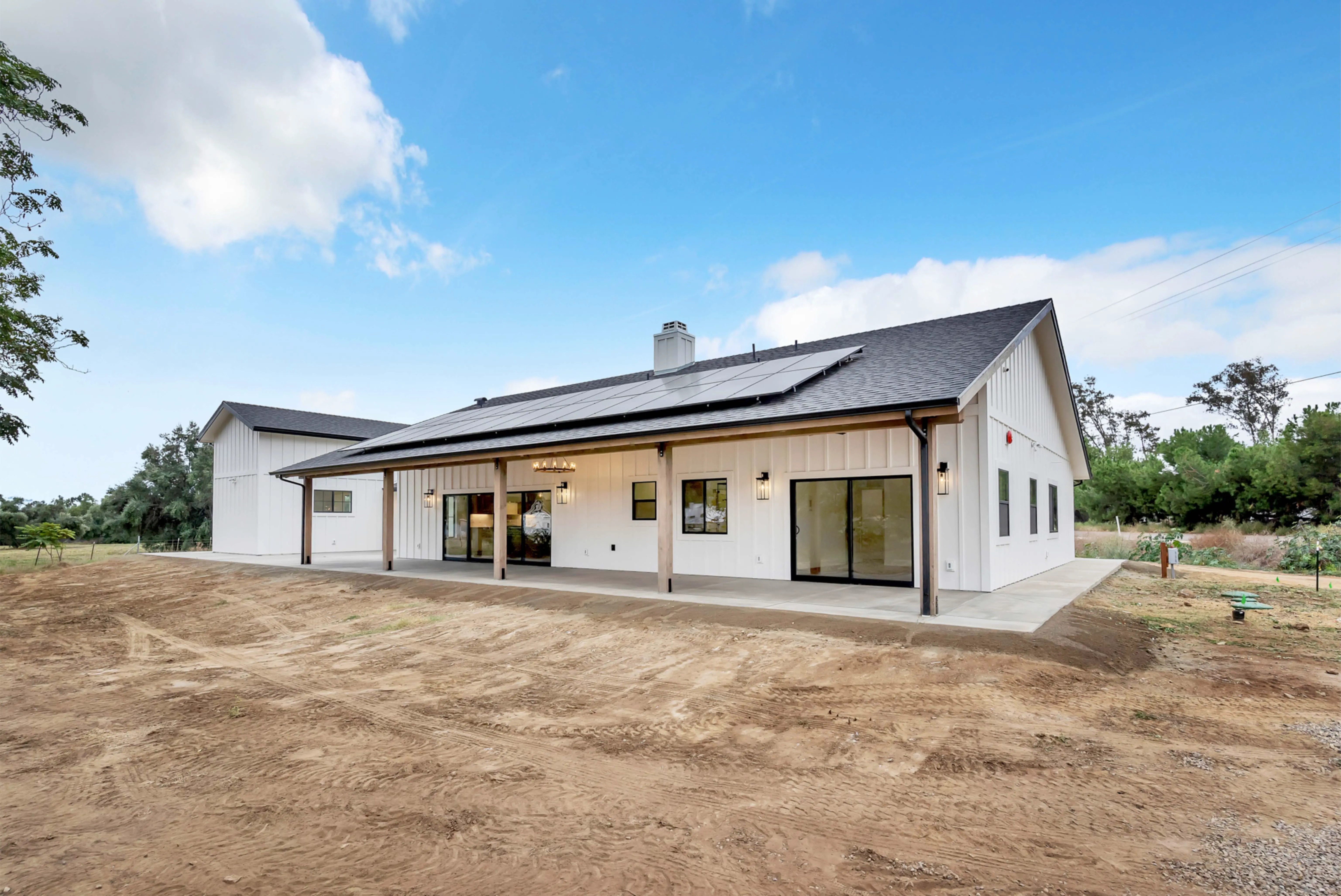 Modern white house with a sloped roof and solar panels, set under a clear blue sky.