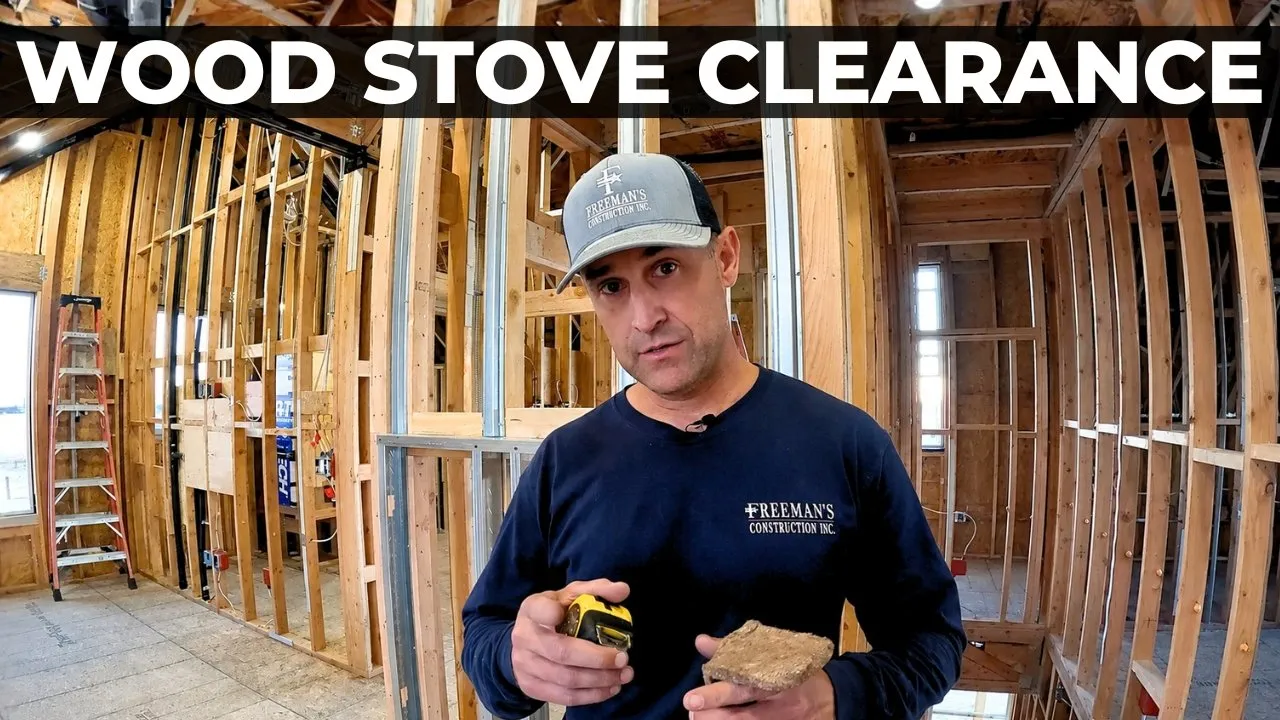 Construction worker inside a partially framed room, holding a tape measure and a piece of wood, with wooden studs all around and a 'Wood Stove Clearance' banner across the top.